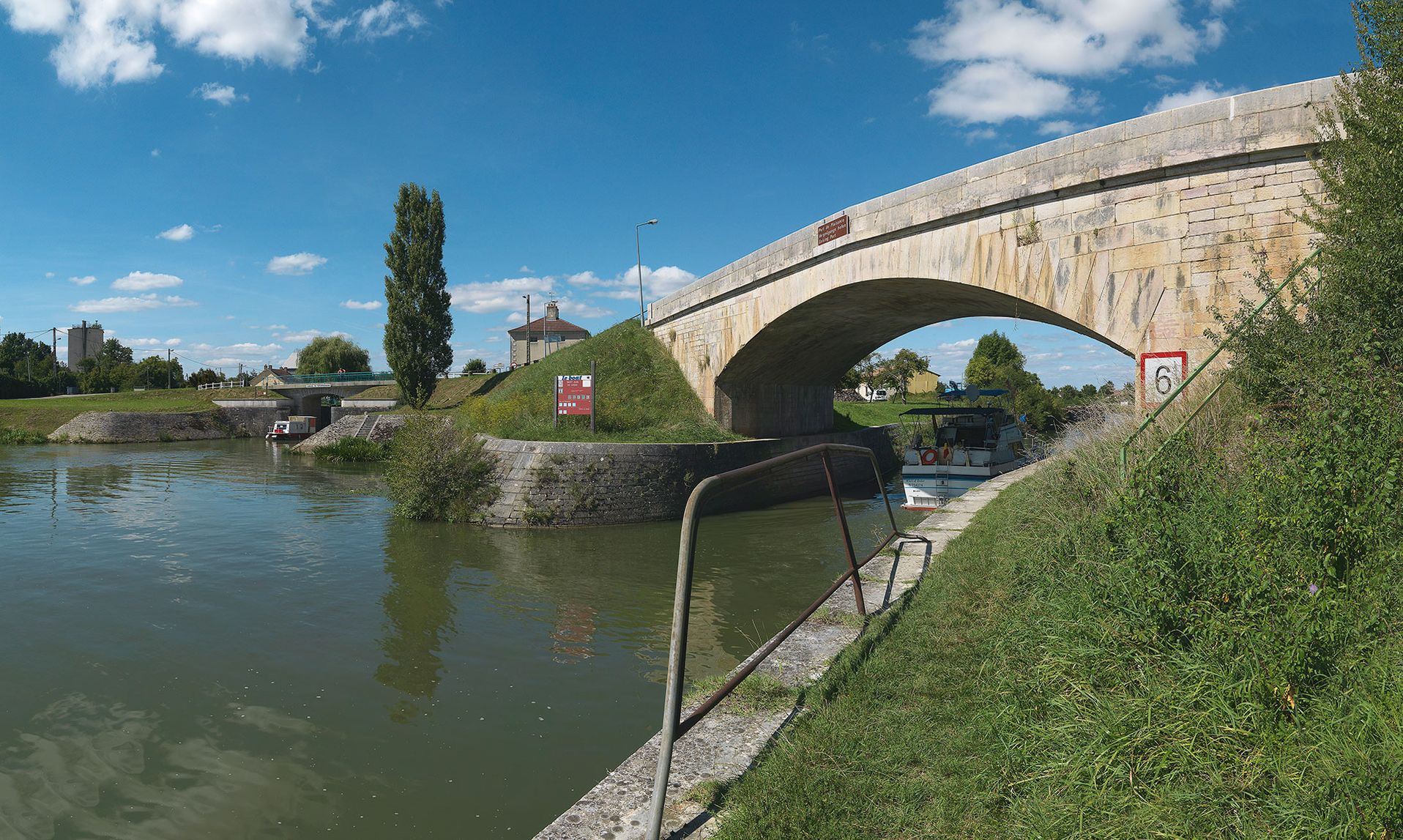 Pont biais en pierre sur le chenal d’accès à la gare d’eau de Saint-Jean-de-Losne. On aperçoit également, l’entrée du canal de Bourgogne, avec le pont sur l’écluse 76 du versant Saône.